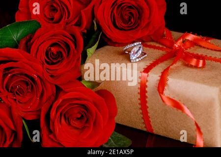 Geschenk und Ring mit schönen roten Rosen auf schwarzem Hintergrund. Valentinstag-Konzept. Stockfoto