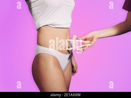 Nahaufnahme des Bauches der jungen attraktiven Frau. Nutritionist Hand Messung Körper Fett Taille Schicht mit Caliper auf rosa Farbverlauf Hintergrund Stockfoto