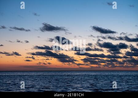 Blick auf die untergehende Sonne, die auf dem Meer scheint und am Strand reflektiert wird, Wolken mit sonnenglänzenden Rändern. Querformat. Hochwertige Foto zeigt Konzept der Freiheit und Träume Stockfoto