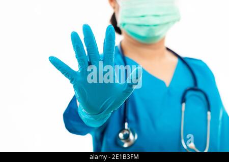 Weibliche Krankenschwester mit Stethoskop setzt Gummihandschuhe und trägt medizinische Gesichtsmaske, Frau Arzt in blauen Uniform zeigen Hand Stop-Zeichen, Studio erschossen isola Stockfoto