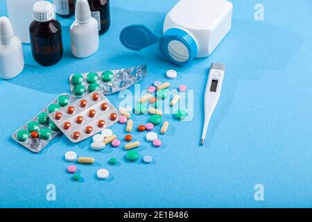 Verschiedene medizinische Medikamente, Thermometer, Spritze, Spray, Flaschen von Tropfen, Sirup, verstreut bunte Tabletten, Kapseln Stockfoto