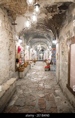 Touristen kaufen Souvenirs aus Geschäften zwischen den Bögen der Altstadt von Kotor, die nachts von Hängelampen beleuchtet werden. Stockfoto