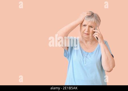Gestresste ältere Frau, die mit dem Handy auf farbigem Hintergrund spricht Stockfoto