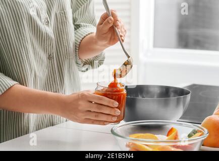 Frau Gießen leckere Pfirsichmarmelade aus der Schüssel in das Glas Stockfoto