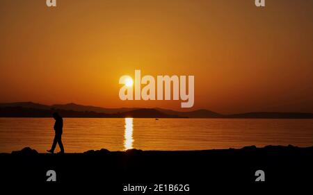Silhouette des Mannes in der Nähe zu Fuß am Strand bei Sonnenuntergang Während der goldenen Stunde Stockfoto