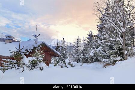 Schöne Aussicht auf eine hölzerne Berghütte in der frischen Schnee mit Tannen bei Sonnenuntergang Stockfoto