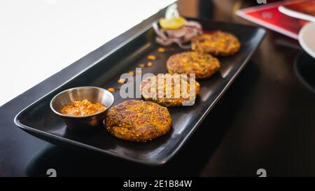 Selektive Konzentration von Quinoa-Patties mit rotem Pfeffer auf einem schwarzen Serviertablett serviert Stockfoto