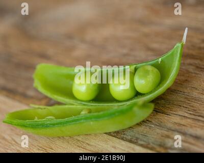 Gemüse, ein Trio von grünen Erbsen in einer offenen Hülse auf einem Holztisch, in einem australischen Garten selbst angebaut. Stockfoto