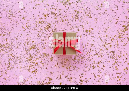 Ein Geschenk in einer Schachtel auf rosa festlichem Hintergrund mit goldenem Konfetti. Draufsicht, flach liegend. Stockfoto