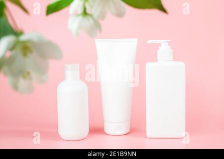 Set von Kosmetik für die Hautpflege Gesicht, Körper. Weiße leere Kosmetikflaschen und Tube auf Glas Podium und blühenden Zweig, rosa Hintergrund. Natürliche Organi Stockfoto