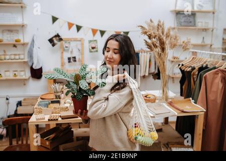 Heitere Frau in ökologischen Shop posiert für ein Foto mit Netzbeutel und Topfpflanze Stockfoto