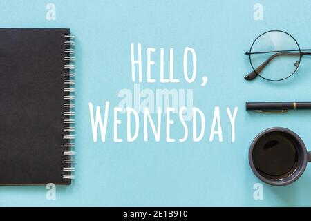 Hallo Mittwoch Worte in schwarzem Notizblock, Stift, Tasse Kaffee und reeding Gläser auf blauem Hintergrund. Konzept Happy Wednesday. Draufsicht Flat Lay. Stockfoto
