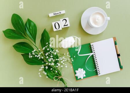 Holzwürfel Kalender März 2. Öffnen Sie leeren Notizblock, Tasse Kaffee, Blumenstrauß auf grünem Hintergrund. Konzept Hello Spring Creative Draufsicht Flat Lay Stockfoto