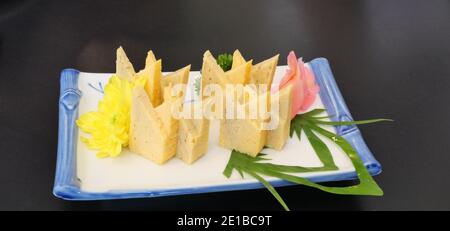 Tamagoyaki oder Sushi süßes Ei mit rot eingelegtem Ingwer in einer weißen quadratischen Keramikplatte auf schwarzem Hintergrund, wunderschön dekoriertes japanisches Essen Stockfoto