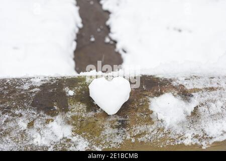 Ein Herz aus Schnee liegt auf einem Holzgeländer, vor dem Hintergrund einer Winterlandschaft mit einem Fluss. Hochwertige Fotos Stockfoto