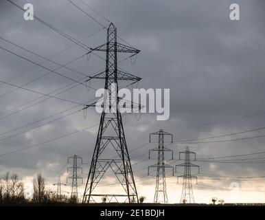 Stromleitungen und Pylonen überqueren Landschaft grau bedeckt bedrohlichen Himmel, Großbritannien Stockfoto
