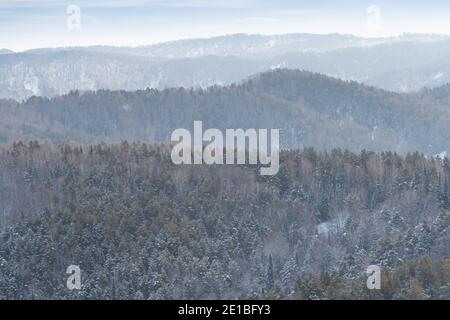 Sanfte Hänge der Waldhügel sind mit ersten Schnee bedeckt. Blick auf Bergtäler und Bergrücken am Horizont. Stockfoto