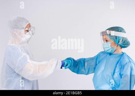 Junge Ärzte begrüßen Fäuste in Schutzkleidung auf grauem Hintergrund. Pandemiebegrüßung, Konzept der sozialen Distanz. Stockfoto