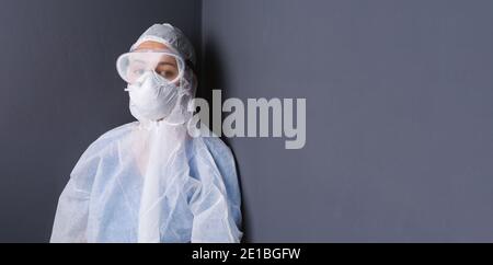 Banner. Ein Arzt in Schutzkleidung, Schutzbrille in einer grauen Wand mit Seitenraum. Das Konzept der Bekämpfung des Coronavirus. Stockfoto