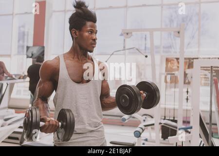 Schöner afrikanischer Sportler, der konzentriert aussieht und schwere Hanteln im Fitnessstudio hebt. Attraktiver männlicher Athlet beim Training mit Gewichten im Sportstudio, Kopie Stockfoto