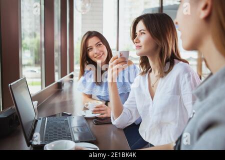 Gruppe von schönen fröhlichen Frauen genießen Morgen Kaffee zusammen im Café. Fröhliche Freundinnen, die bei einer Tasse Tee im Café reden Stockfoto