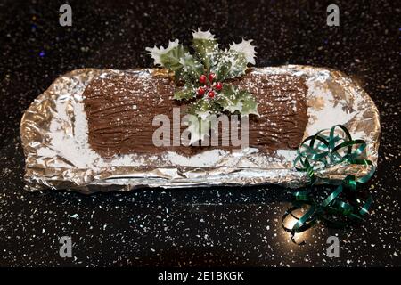 Nahaufnahme von köstlichen hausgemachten Schokolade überzogene Schweizer Brötchen Kuchen mit Puderzucker und Stechpalme zur Dekoration Stockfoto