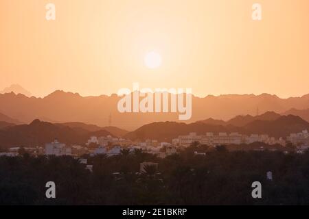 Sonne über der Altstadt gegen die Bergkette. Nizwa im Sultanat Oman bei herrlichem Sonnenuntergang. Stockfoto