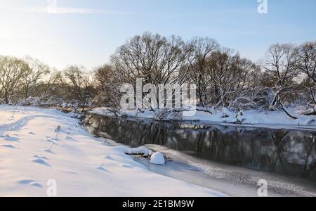 Frostige Winterszene mit Waldfluss an einem sonnigen Morgen. Wunderschöne schneebedeckte Bäume im Schein der aufgehenden Sonne. Stockfoto