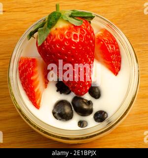 Frische Erdbeeren und Heidelbeeren im Glas Joghurt oder Joghurt auf Holz Hintergrund Stockfoto