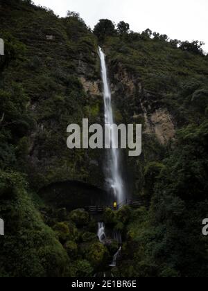 Junger Mann in gelber Jacke vor El Chorro De Giron Wasserfall Kaskade Katarakt bei Cuenca Azuay Ecuador in Südamerika Stockfoto