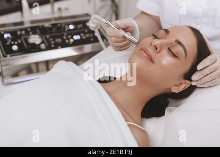 Professionelle cosmetologit Durchführung Mikrodermabrasion Verfahren auf dem Gesicht einer weiblichen Klientin. Schöne junge Frau bekommen Gesicht Haut Peeling t Stockfoto