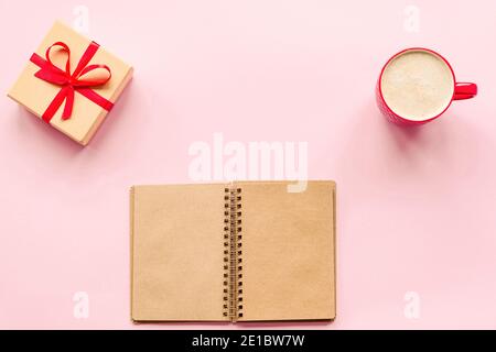 Tasse Kaffee, Geschenk in einer Box und ein Notizbuch auf einem rosa Hintergrund. Liebeskonzept, Valentinstag. Draufsicht, flach liegend. Stockfoto