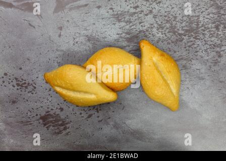 Drei frisch gebackene Bolillo-Brötchen auf grau meliertem Hintergrund. Stockfoto