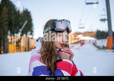 Portrait von Happy Pretty Kaukasische Frau im Ski-Outfit und mit Snowboarding Maske auf dem Kopf. Porträt einer fröhlichen blonden Frau im Skigebiet Stockfoto