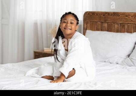 Schöne kleine afroamerikanische Mädchen im Bademantel entspannend auf dem Bett Nach dem Duschen Stockfoto