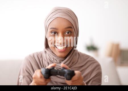 Portrait der glücklichen muslimischen Frau in Hijab halten Joystick, spielen Videospiel zu Hause Stockfoto