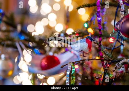 Weihnachtsbaum mit einer blauen medizinischen Maske mit verschiedenen Dekorationen in ihm geschmückt, defokussierte Lichter auf dem Hintergrund Stockfoto