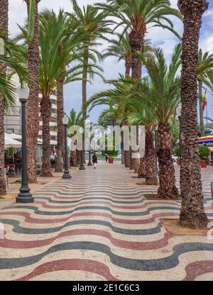 Explanada de España, die Strandpromenade von Alicante, die mit marmorgemusterten Wellen gepflastert ist, flankiert von Palmenreihen, Costa Blanca, Spanien. Stockfoto