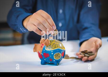 Der junge Finanzanalyst steckt Geld in ein kleines Schwein. Münzen in die Kasse einführen. Geld sparen in kleinen Mengen. Stockfoto