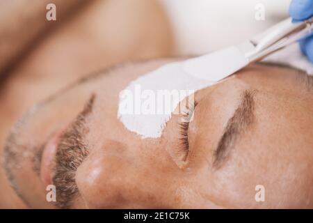 Nahaufnahme eines bärtigen reifen Mannes, der im Spa-Center Gesichtsmasken erhält. Kosmetikerin Anwendung Gesichtsmaske auf mittleren Alters männlichen Kunden. Reso Stockfoto