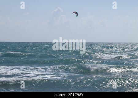 Kiteboarder wird von einem Power Kite in Zypern, Europa in der Nähe des berühmten Pissouri Strandes über Wasser gezogen. Wunderbarer Tag mit Wasseraktivität. Aktiver Lebensstil. Stockfoto