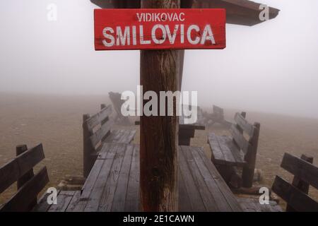 Smilovica Aussichtspunkt, mit rotem Schild, Holzbänke und Tische, an einem nebligen, nebligen Tag Stockfoto