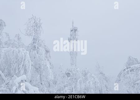 Eisbedeckte Zelle Turm über einem verschneiten Wald auf Ein Berg gegen einen Winterhimmel Stockfoto