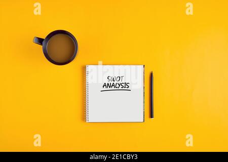 SWOT-Analyse auf Notizbuch mit Stift und Kaffeetasse auf gelbem Hintergrund geschrieben. Konzept der Marketingstrategie. Stockfoto