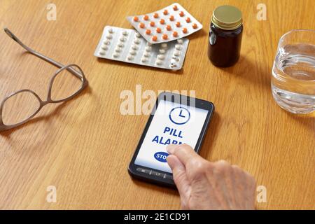 Pille Alarm App auf Handy, Handy oder Smartphone, mit Wasserglas, Brille, Medizin und die Hand einer älteren Frau. Stockfoto