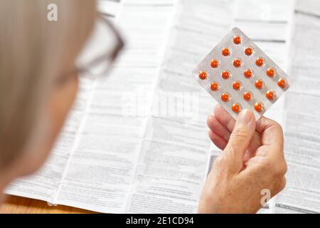 Ältere Frau hält ein Blatt oranger Pillen vor einer riesigen Drogenpackung. Gesundheitswesen und Medizin Konzept. Stockfoto