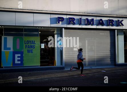 Loughborough, Leicestershire, Großbritannien. Januar 2021. Eine Frau rennt bei der dritten nationalen Covid-19-Sperre an einem geschlossenen Primark-Laden vorbei. Credit Darren Staples/Alamy Live News. Stockfoto