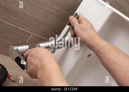Installieren eines Waschbecken im Badezimmer auf einer hölzernen Arbeitsplatte. Installation des Mischers. Sanitäranlagen. Stockfoto