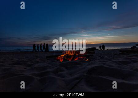 Nicht erkennbare Menschen feiern Sommersonnenwende mit Lagerfeuer am Strand Stockfoto