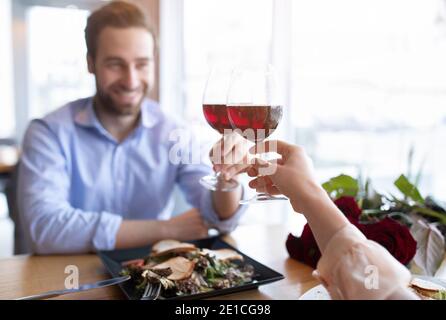 Romantisches junges Paar mit Gläsern Rotwein toasting einander, feiern Valentinstag im Restaurant Stockfoto